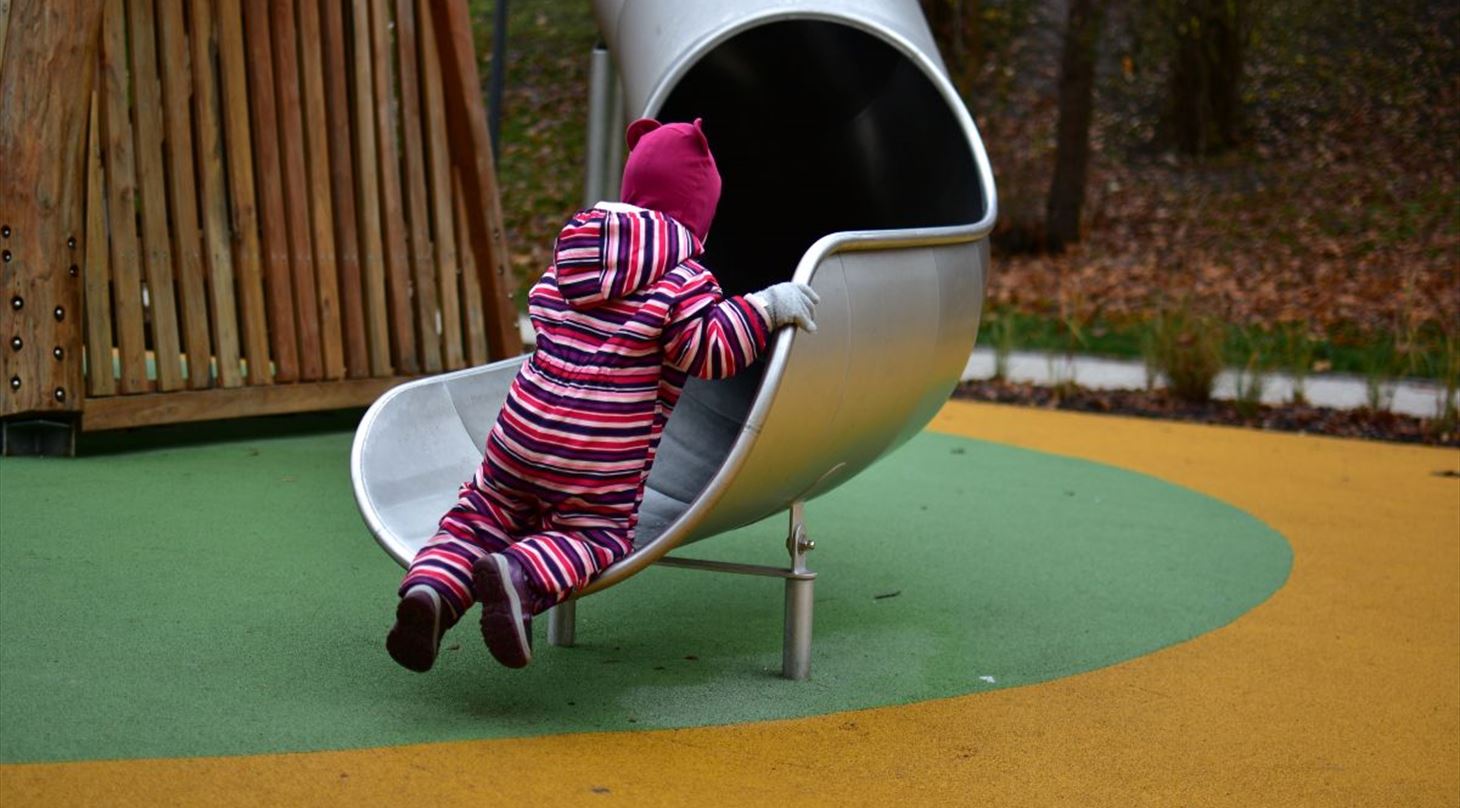 En pige leger p� en legeplads med underlag og rutsjebane